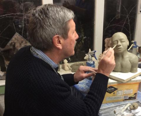 Student sculpting with clay, and making a small  portrait bust