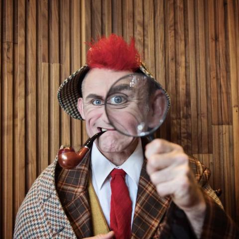 Tweedy the clown looks through a magnifying glass