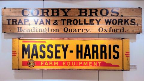 Two narrow but wide signs. Top sign is corby bros, trap, van and trolley works, headington quarry, oxford. The sign beneath is Massey - Harris