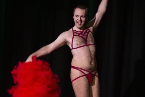 Frisky Whispers a Queerlesque performer in harness and underwear with feather fan 