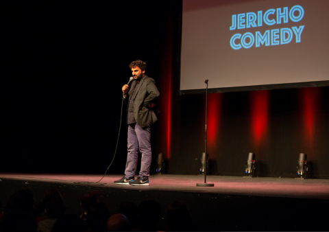 Nish Kumar on stage in front of a projection that says 'Jericho Comedy'.