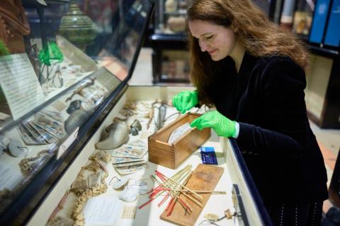 Woman wearing black clothes and bright green gloves places objects in open museum display case
