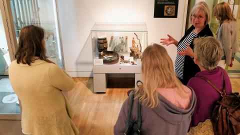 A member of staff talks to a group about objects in a display case.